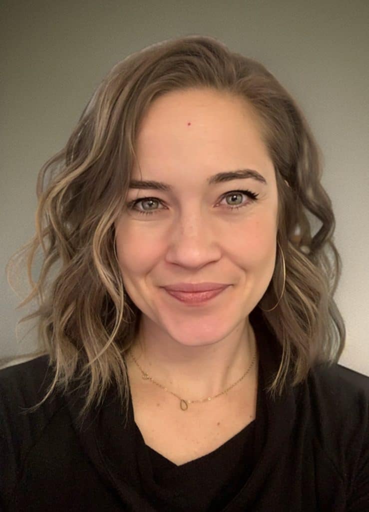 White woman with light brown wavy hair smiles at the viewer